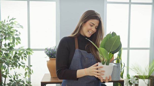 Hymyilevä nainen, jolla on kasvi kirkkaassa kukkakaupassa, herättäen tuoretta sisätunnelmaa - Valokuva, kuva
