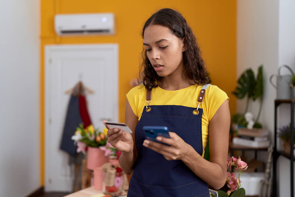 Joven florista afroamericana mujer usando teléfono inteligente con tarjeta de crédito en la tienda de flores - Foto, Imagen
