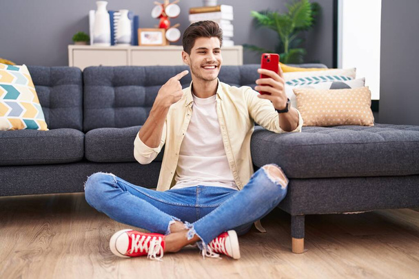 Giovane uomo ispanico fare videochiamata con smartphone sorridente felice puntando con mano e dito  - Foto, immagini