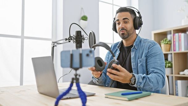 Latino mies parta hosting podcast moderni studio, kannettava tietokone ja mikrofoni pöydällä. - Valokuva, kuva