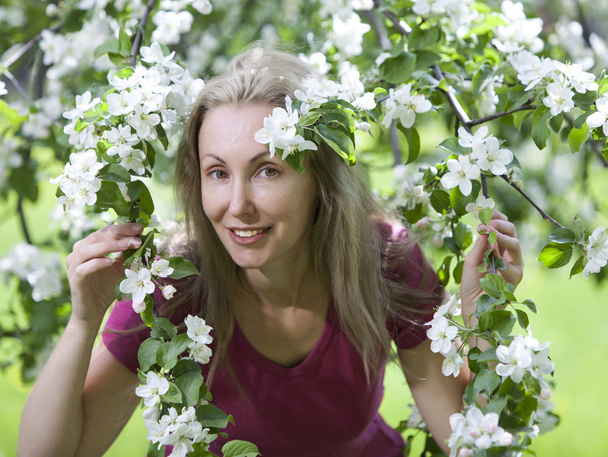 Young attractive woman standing near the blossoming apple tree - Fotoğraf, Görsel