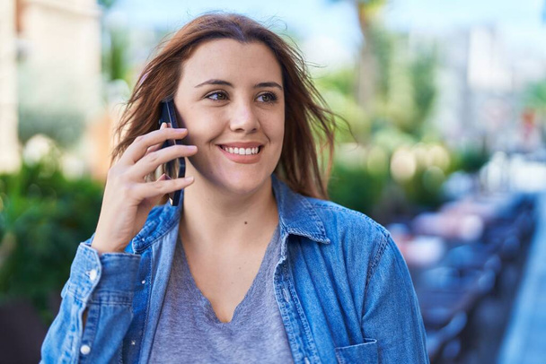 Молодая красивая женщина плюс размер улыбается уверенно разговаривая на смартфоне на террасе кафе - Фото, изображение