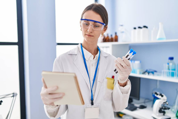 Young caucasian woman scientist holding test tubes reading notebook at laboratory - Photo, image