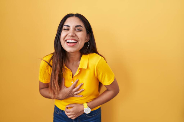 Mujer árabe joven de pie sobre fondo amarillo sonriendo y riendo en voz alta porque broma loca divertida con las manos en el cuerpo.  - Foto, Imagen