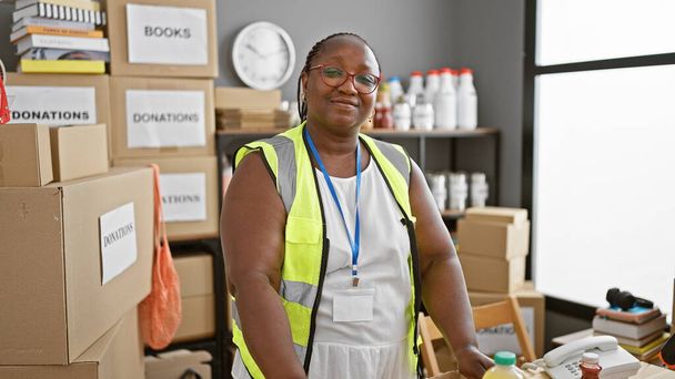 Confident african american woman volunteer, smiling and standing proud at charity center. working in unity, she personifies altruism in her reflective vest. - Photo, Image