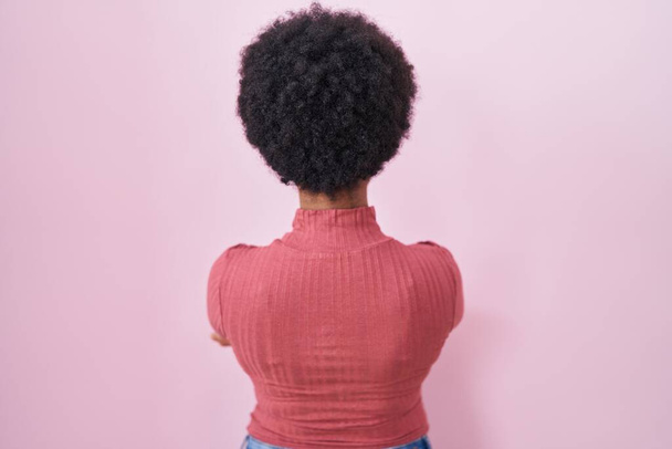 Gyönyörű afrikai nő göndör haj felett áll rózsaszín háttér álló hátrafelé néz félre keresztbe karok  - Fotó, kép