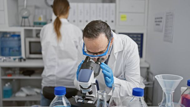 Kendini işine adamış iki bilimadamı, takım arkadaşları laboratuvarda birlikte çalışıyorlar. Mikroskop kullanarak ciddi araştırmalarla meşguller. Tıp biliminde yeni analizler keşfediyorlar.. - Fotoğraf, Görsel