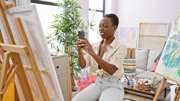Впевнена афроамериканська жінка-художниця, малюнок із зображення, зробленого зі своїм смартфоном у затишній художній студії - Фото, зображення