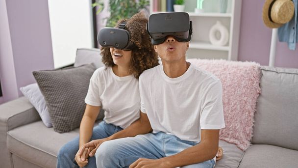 Εκπληκτικό όμορφο ζευγάρι μαζί στο σπίτι, βαθιά ερωτευμένοι, παίζοντας σοβαρά βιντεοπαιχνίδια χρησιμοποιώντας φουτουριστικά γυαλιά εικονικής πραγματικότητας στο σαλόνι - Φωτογραφία, εικόνα