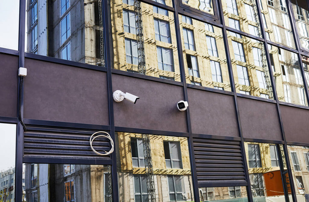 az épület tükrös homlokzata biztonsági kamerákkal és az építés alatt álló épület tükröződése - Fotó, kép