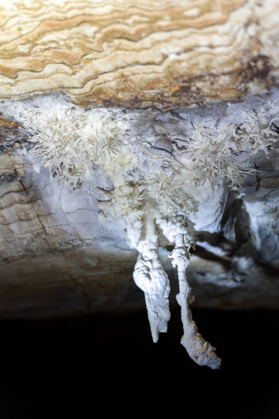 Нетронутые белые сталактиты против слоистых камней в пещере. - Фото, изображение