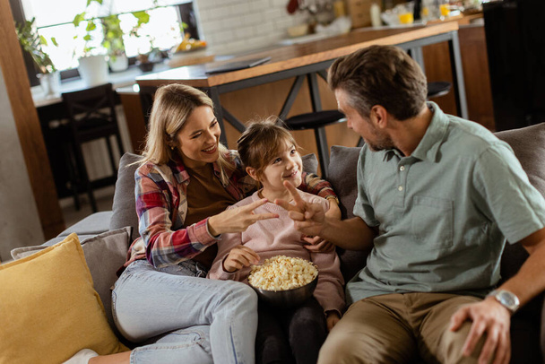 Eine fröhliche Familie sitzt auf dem Sofa und unterhält sich verspielt mit einer Schüssel Popcorn - Foto, Bild
