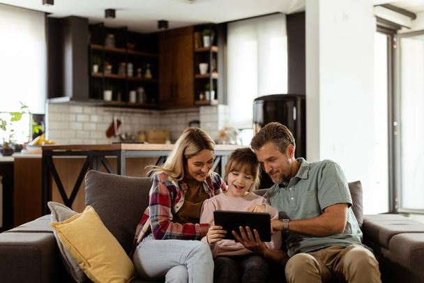 Freudige Familie teilt einen Moment rund um ein digitales Tablet, mit Lächeln und Zweisamkeit in einer warmen Umgebung zu Hause - Foto, Bild