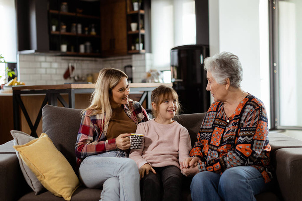 Três gerações de mulheres gostam de rir e conversar em um sofá confortável sala de estar - Foto, Imagem