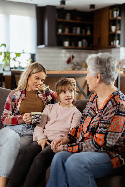 Três gerações de mulheres gostam de rir e conversar em um sofá confortável sala de estar - Foto, Imagem