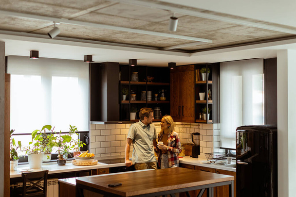 Escena conmovedora se desarrolla en una cocina doméstica como una pareja comparte un abrazo cariñoso, rodeado de la tranquilidad de su casa al final del día - Foto, Imagen