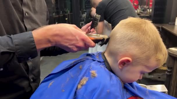 Kampaaja sähköparranajokoneella leikata poikien hiukset. Pikkupoika parturissa parturissa. Sulje se. - Materiaali, video