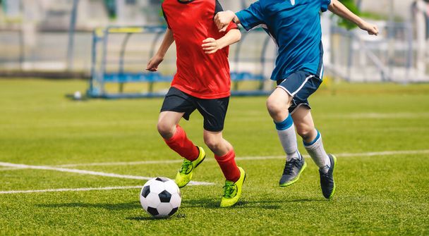 İki futbolcu bir düelloda bir futbol topunu kovalıyor. Çocuklar çimen sahasında futbol oynuyor. Futbol akademisi oyuncuları okul turnuvasında yarışıyorlar. Genç futbolcular koşuyor ve topa vuruyor - Fotoğraf, Görsel