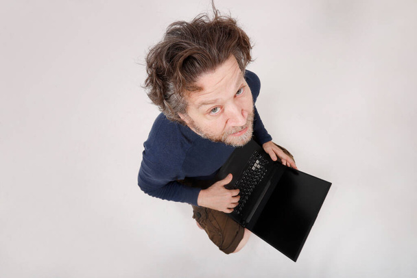 Mann arbeitet an seinem Laptop und blickt in Kamera klaren Hintergrund - Foto, Bild