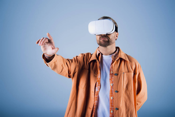 Un hombre con una chaqueta naranja se adentra en el Metaverse con un auricular de realidad virtual en un entorno de estudio. - Foto, imagen