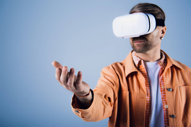 Un uomo con una camicia arancione è immerso nel metaverso mentre sperimenta la realtà virtuale in un ambiente da studio. - Foto, immagini