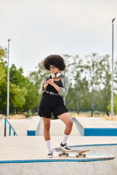 Um adolescente afro-americano com cabelo encaracolado confiantemente de pé com um skate em um parque de skate. - Foto, Imagem