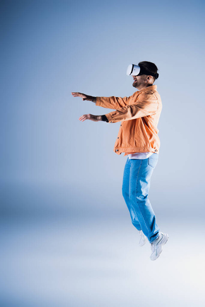 Человек в VR гарнитуре энергично прыгает в студию, демонстрируя свои акробатические навыки в стильной шляпе.. - Фото, изображение