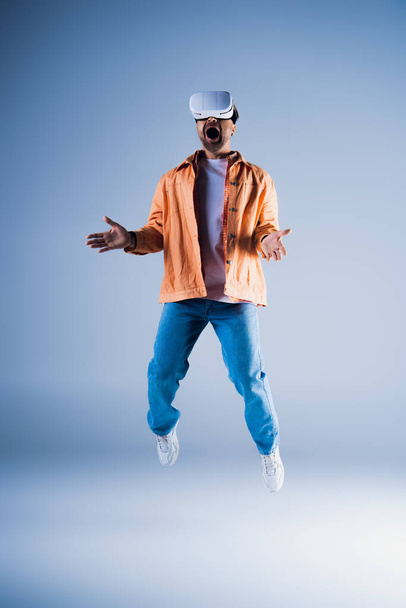 A man in a vibrant orange jacket is caught mid-air, showcasing his energetic leap in a studio setting. - Photo, Image