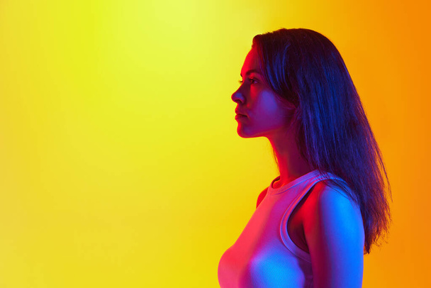Portrait latéral d'une jeune femme confiante posant dans une lumière vive au néon sur fond de studio jaune orangé Concept d'émotions humaines, d'expression de soi, d'expression faciale, de beauté, de jeunesse. Publicité - Photo, image