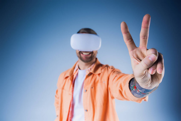 Ein Mann in orangefarbenem Hemd mit Augenbinde im Studio, der die Grenzen der Realität durch Virtual Reality erkundet. - Foto, Bild