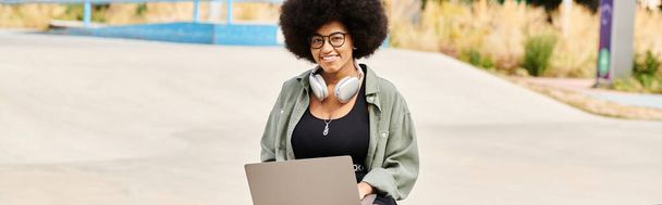 Una mujer con un afro sostiene una computadora portátil, fusionando tecnología y cultura. - Foto, imagen