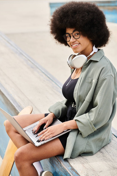 Młoda kobieta z kręconymi włosami relaksuje się na ławce, pochłonięta laptopem w tętniącym życiem skateparku. - Zdjęcie, obraz