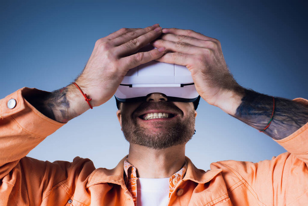 Un uomo che indossa una camicia arancione in un ambiente da studio, immerso in un'esperienza di realtà virtuale. - Foto, immagini