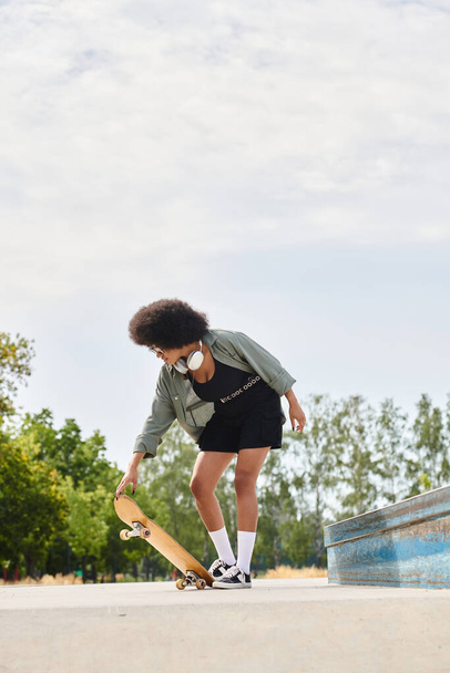 Афроамериканка с вьющимися волосами скользит на скейтборде в гладком черном платье в открытом скейт-парке. - Фото, изображение