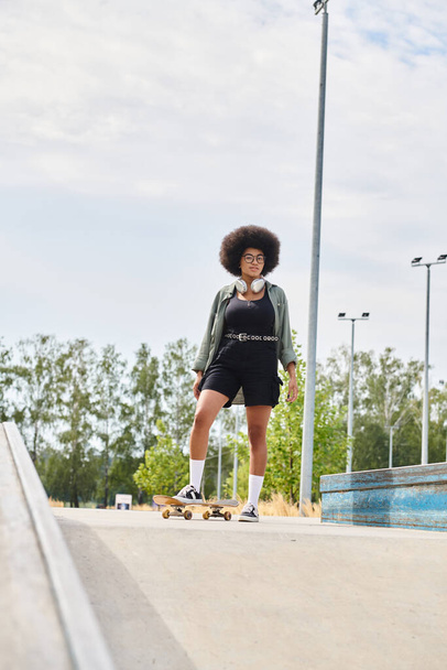 Nuori afroamerikkalainen nainen, jolla on kiharat hiukset, rullalautailee luottavaisesti kaupungin jalkakäytävällä aurinkoisena päivänä.. - Valokuva, kuva