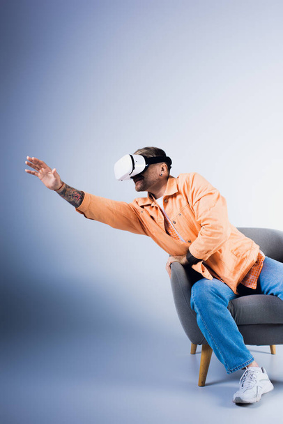 Muž ve VR sluchátkách sedí v křesle se zdviženou rukou, ponořený do virtuálního světa - Fotografie, Obrázek