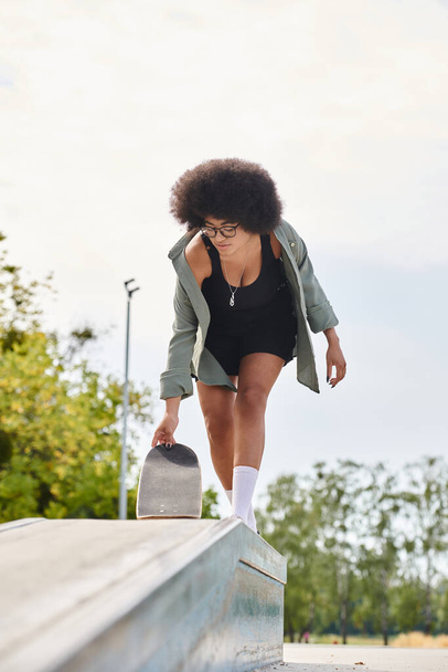 Une jeune Afro-Américaine aux cheveux bouclés glisse sur une planche à roulettes dans un skate park. - Photo, image