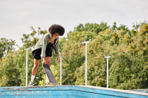 Havuzun kenarında dinamik ve cüretkar bir hareketle kıvırcık saçlı kaykaylı yetenekli bir Afrikalı genç Amerikalı kadın.. - Fotoğraf, Görsel