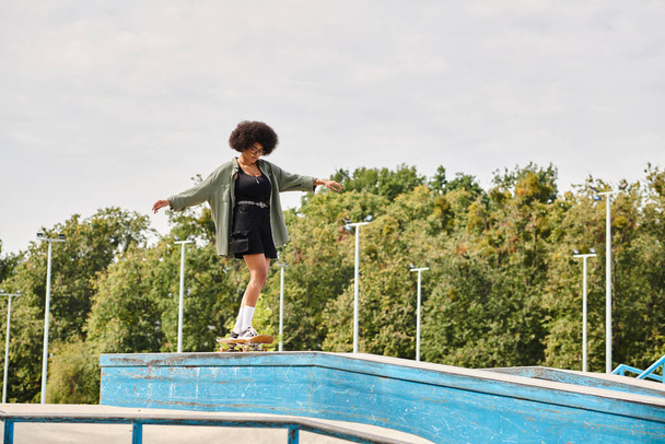 Egy fiatal afro-amerikai nő göndör hajjal ügyesen gördeszkázik a medence szélén egy szabadtéri gördeszka parkban.. - Fotó, kép