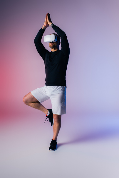 Mies mustassa paidassa ja valkoisissa shortseissa harjoittelee haastavaa joogaa, aiheuttaa itsevarmuutta ja hallintaa studioympäristössä.. - Valokuva, kuva