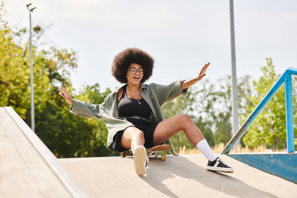 Een jonge Afro-Amerikaanse vrouw met krullend haar rijdt op een skateboard op de zijkant van een helling bij een outdoor skate park. - Foto, afbeelding
