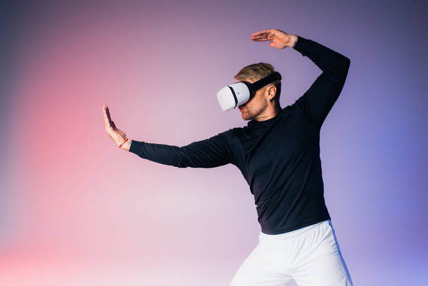 A man in a black shirt and white pants immersed in the metaverse with a VR headset in a studio setting. - Photo, Image