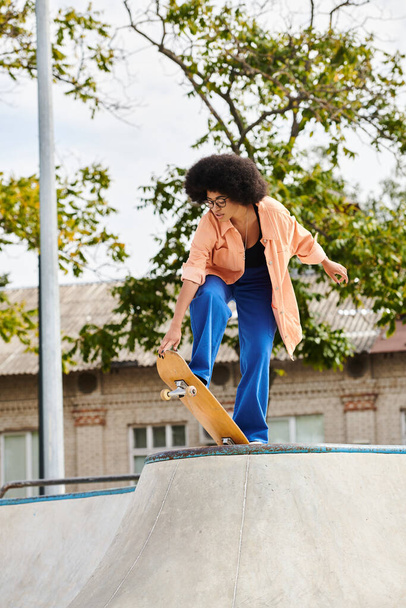 Μια νεαρή Αφροαμερικανή γυναίκα με σγουρά μαλλιά skateboarding επιδέξια σε μια ράμπα σε ένα υπαίθριο πάρκο skate. - Φωτογραφία, εικόνα
