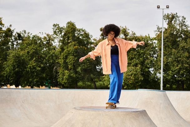 A young African American woman with curly hair confidently rides her skateboard up the side of a ramp at a skate park. - Photo, Image