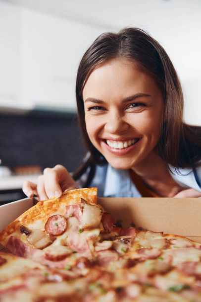 Ευτυχισμένη γυναίκα που κρατάει μια νόστιμη πίτσα με ζαμπόν και τυρί σε ένα κουτί, χαμογελώντας με χαρά - Φωτογραφία, εικόνα
