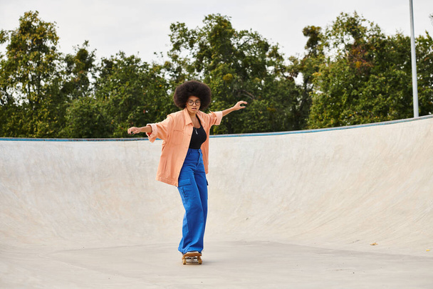 Młoda Afroamerykanka z kręconymi włosami energicznie jeździ na deskorolce po rampie w miejskim skateparku. - Zdjęcie, obraz