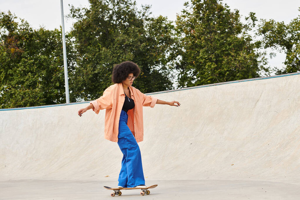 Eine junge Afroamerikanerin mit lockigem Haar fährt in einem Outdoor-Skatepark gekonnt mit einem Skateboard die Seite einer Rampe hinauf. - Foto, Bild