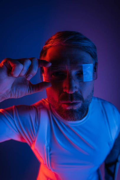 Muž v chytrých brýlích stojí sebevědomě před zářivým červeným a modrým pozadím ve studiu. - Fotografie, Obrázek