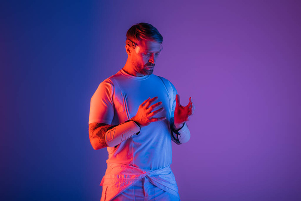 Ein Mann mit smarter Brille steht selbstbewusst in einem Studio vor einem leuchtend violetten und blauen Hintergrund und beschwört ein Gefühl virtueller Realität herauf. - Foto, Bild