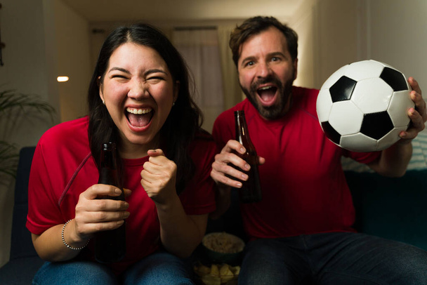 Vidám kaukázusi nő és férfi éljenzi és ünnepli a győzelmet a focicsapat, miközben nézi a játékot a TV-ben otthon - Fotó, kép